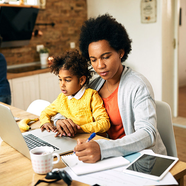 Mom at her laptop writing in her notebook with her daughter on her lap