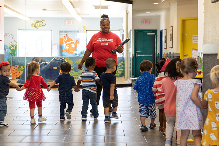 A teacher walking with a group of kids holding hands in the school hallway